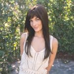 Woman with long dark brown wig outdoors, smiling, natural sunlight.